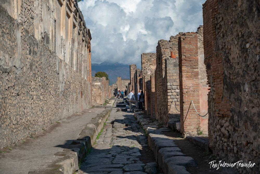 Ancient cobblestone street in Pompeii with ruined brick walls and Mount Vesuvius in the distance