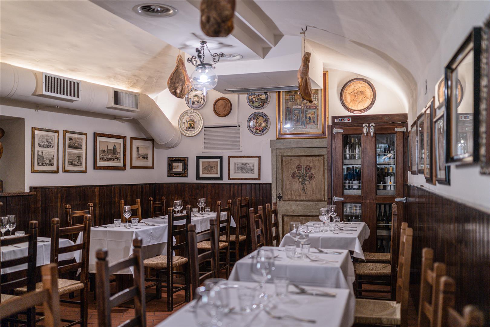 Rustic dining room at Trattoria Il Latini, Florence, with cured hams hanging from vaulted ceilings
