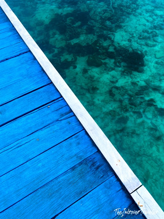 Blue painted wooden dock edge over crystal-clear turquoise waters of Raja Ampat, revealing coral below