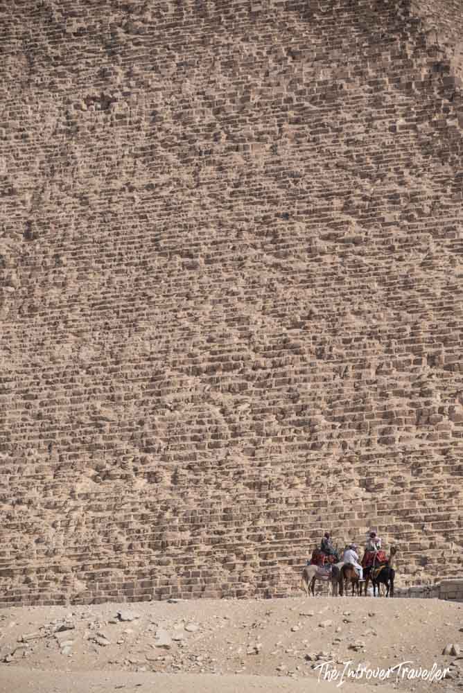 Camel riders dwarfed by the massive limestone blocks of the Great Pyramid of Giza, Egypt