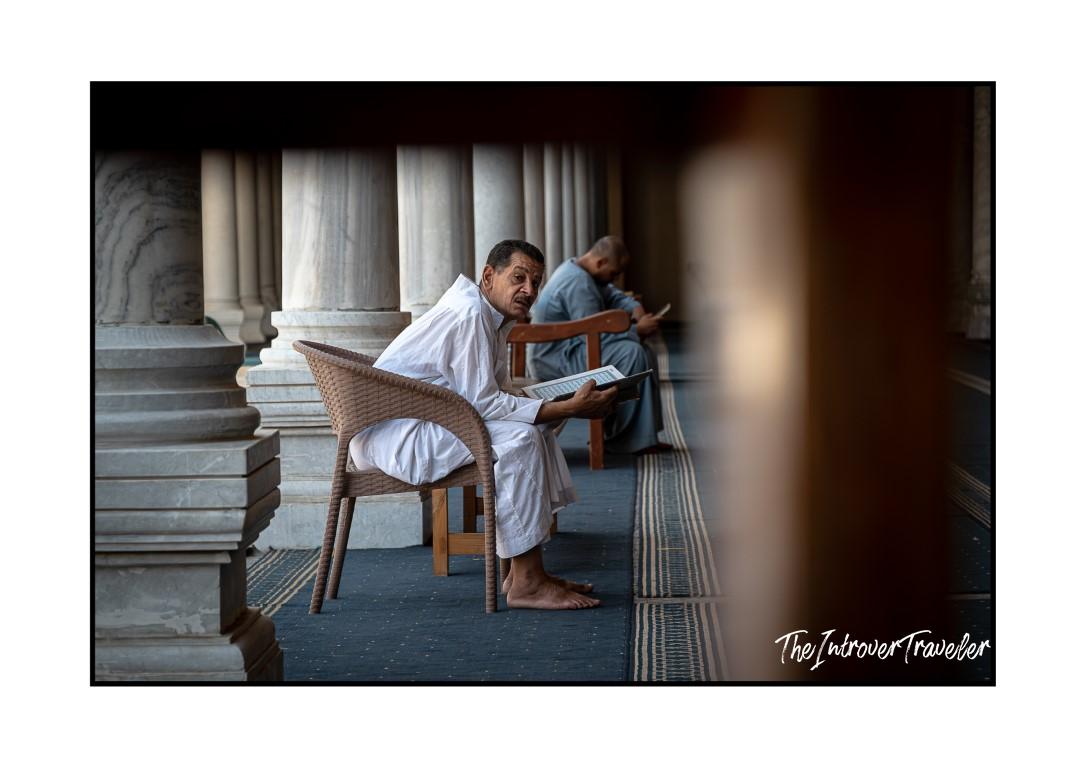 Barefoot worshipper reading the Quran beside marble columns inside an Egyptian mosque