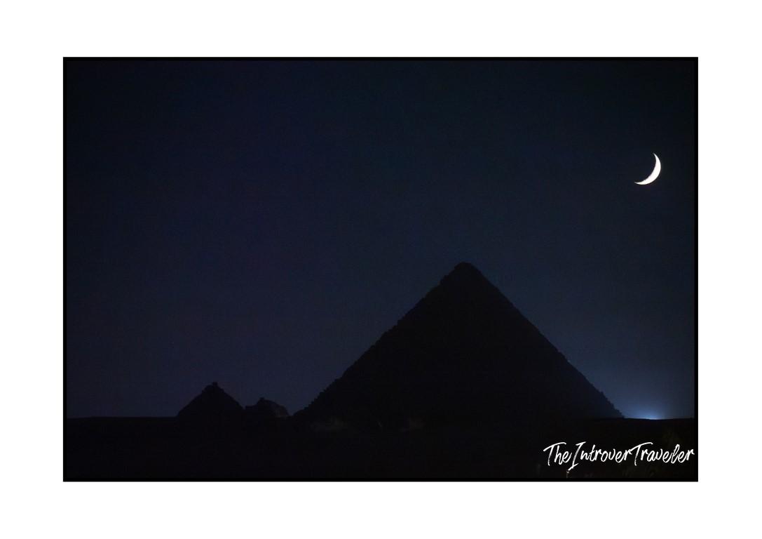 Giza Pyramids silhouetted against a deep blue night sky with a crescent moon, Egypt