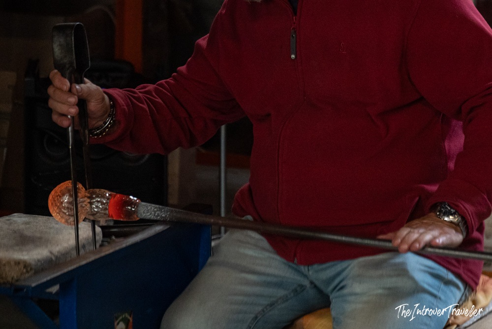 Murano glassmaker shaping molten glass on a blowpipe using iron tongs in a Venice furnace