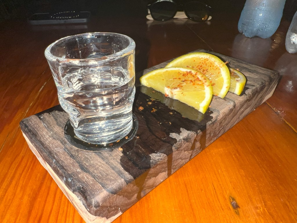 Mezcal shot with chili-dusted orange slices at Kondesa, Cozumel, served on a rustic wood board