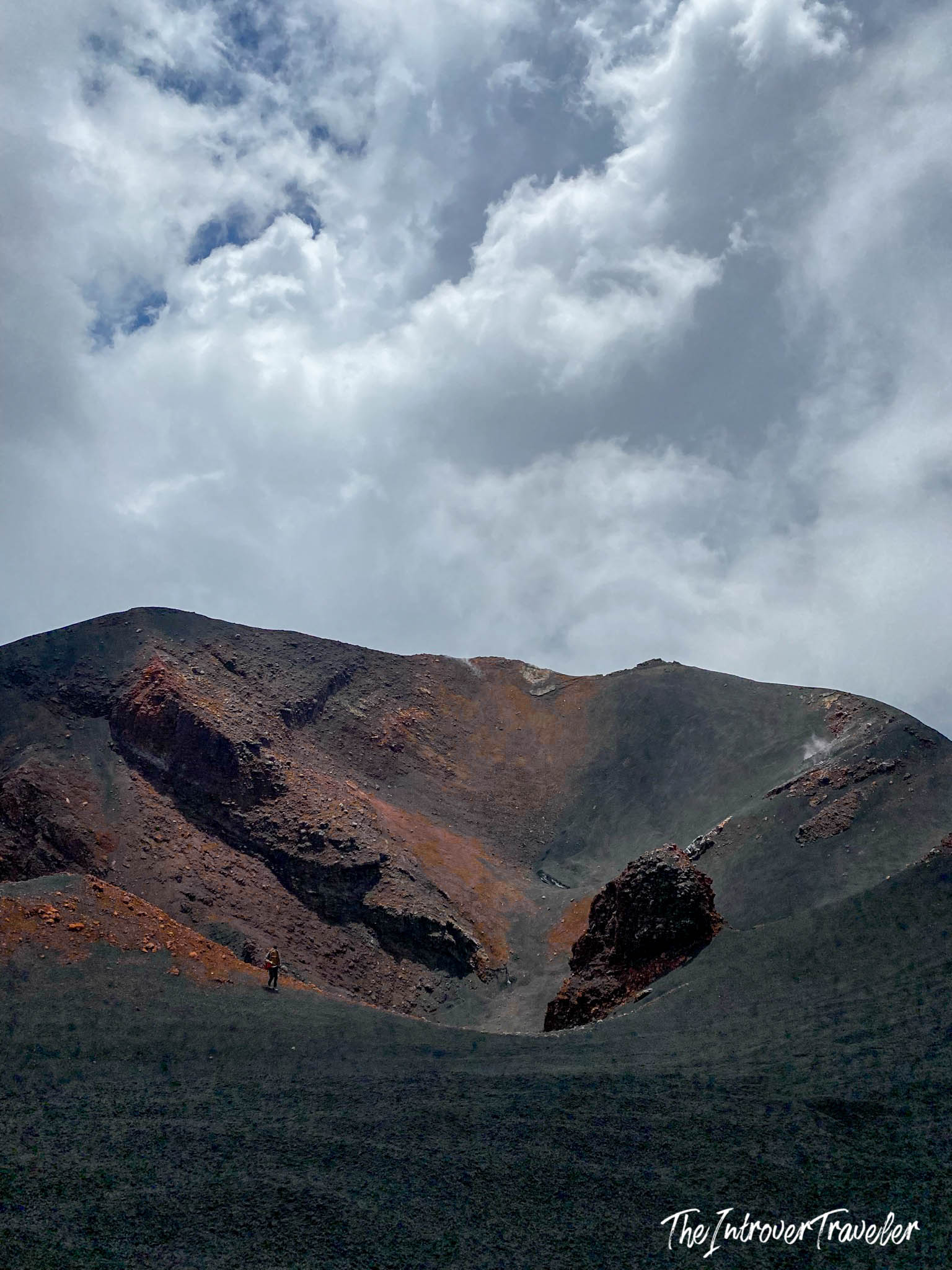 Lone hiker dwarfed by Mount Etna's vast volcanic crater, red lava rock and ash fields, Sicily