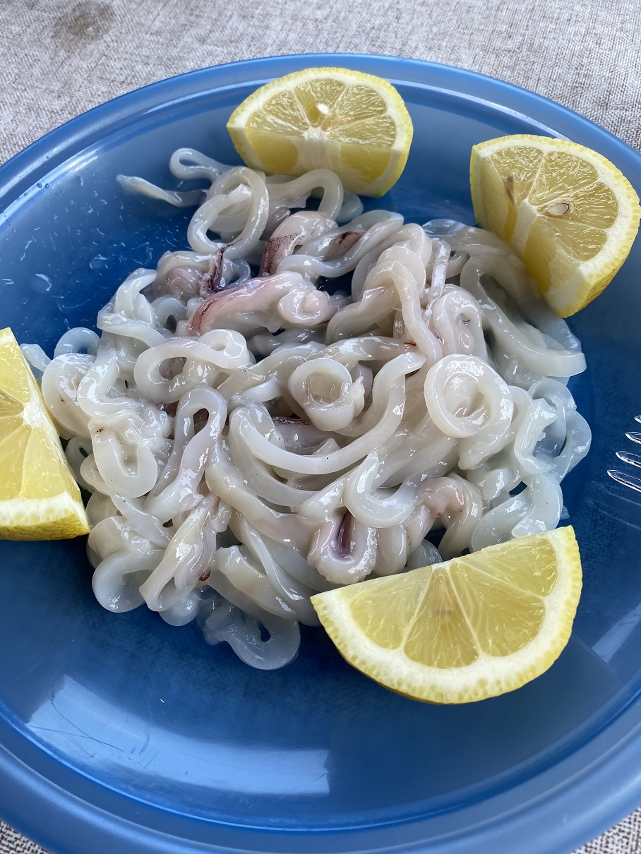 Fresh boiled squid rings with lemon wedges, a seafood specialty served at Capisci in the Three Aci, Sicily