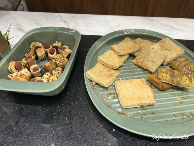 CAC Lounge Cairo Airport snacks: mini sausage rolls and dry crackers on sage green serving dishes