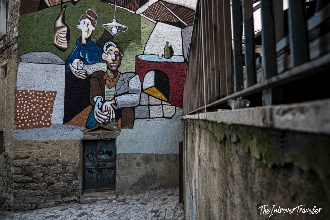 Cubist-style political mural on a stone wall in Orgosolo, Sardinia, depicting two figures indoors