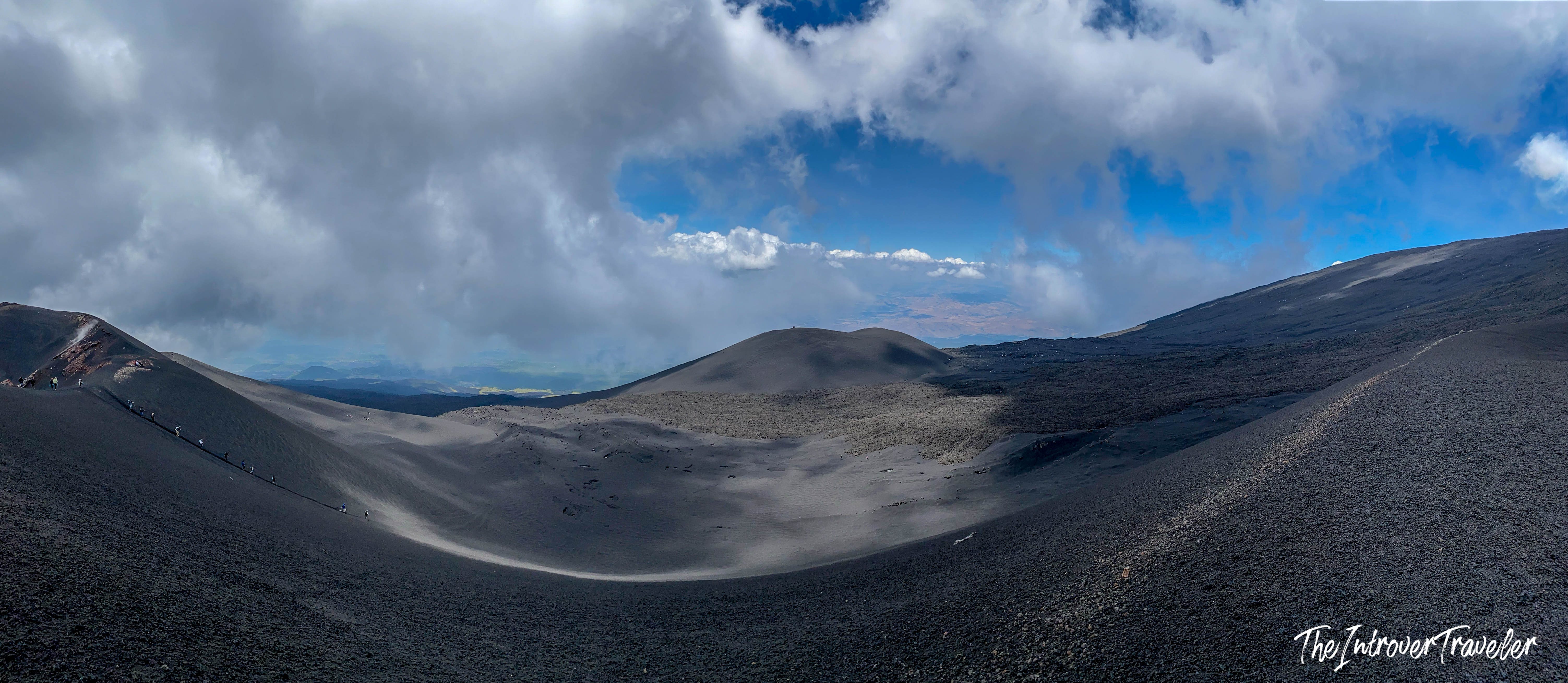 Panoramic view of Mount Etna's black lava landscape, with volcanic craters and hikers on the slopes