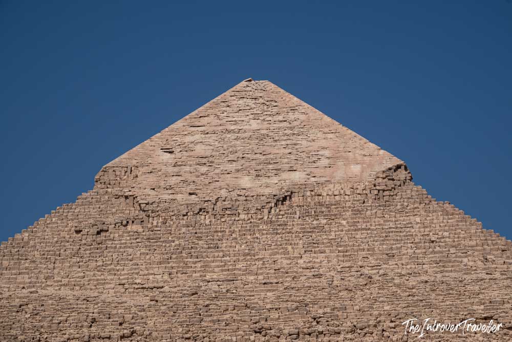 Close-up of the Pyramid of Khafre apex, showing its remaining original limestone casing stones against a clear blue sky.