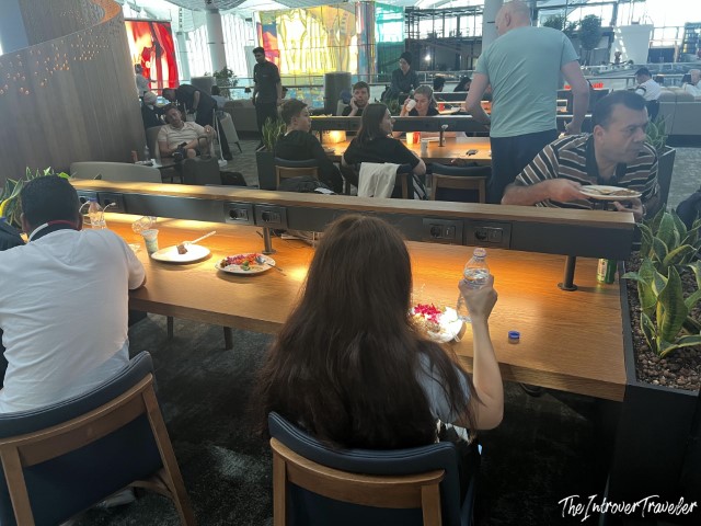Travelers dining at the IGA Lounge in Istanbul Airport, with food and drinks on wooden tables