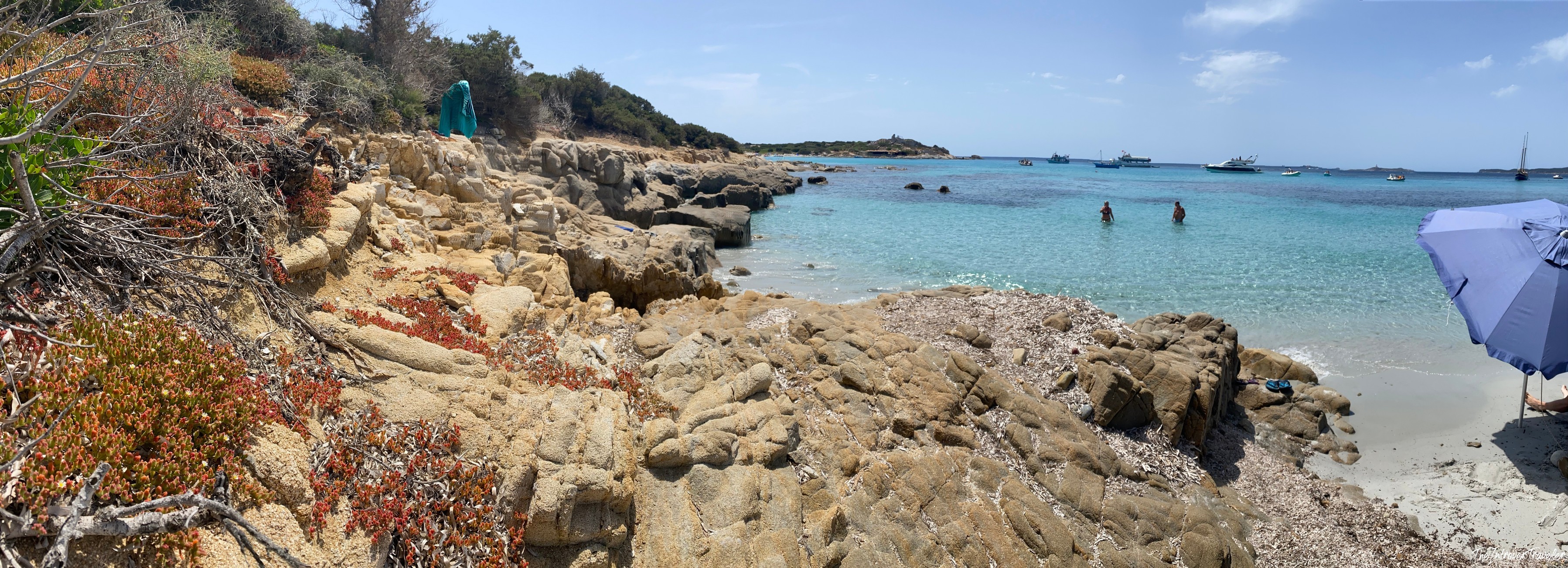Rocky shoreline with turquoise cove waters and boats anchored off a south Sardinia beach