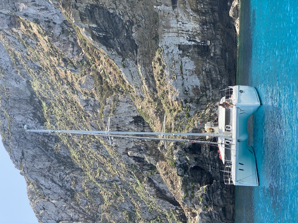 White catamaran anchored in turquoise waters near the dramatic limestone cliffs of Marettimo, Egadi Islands