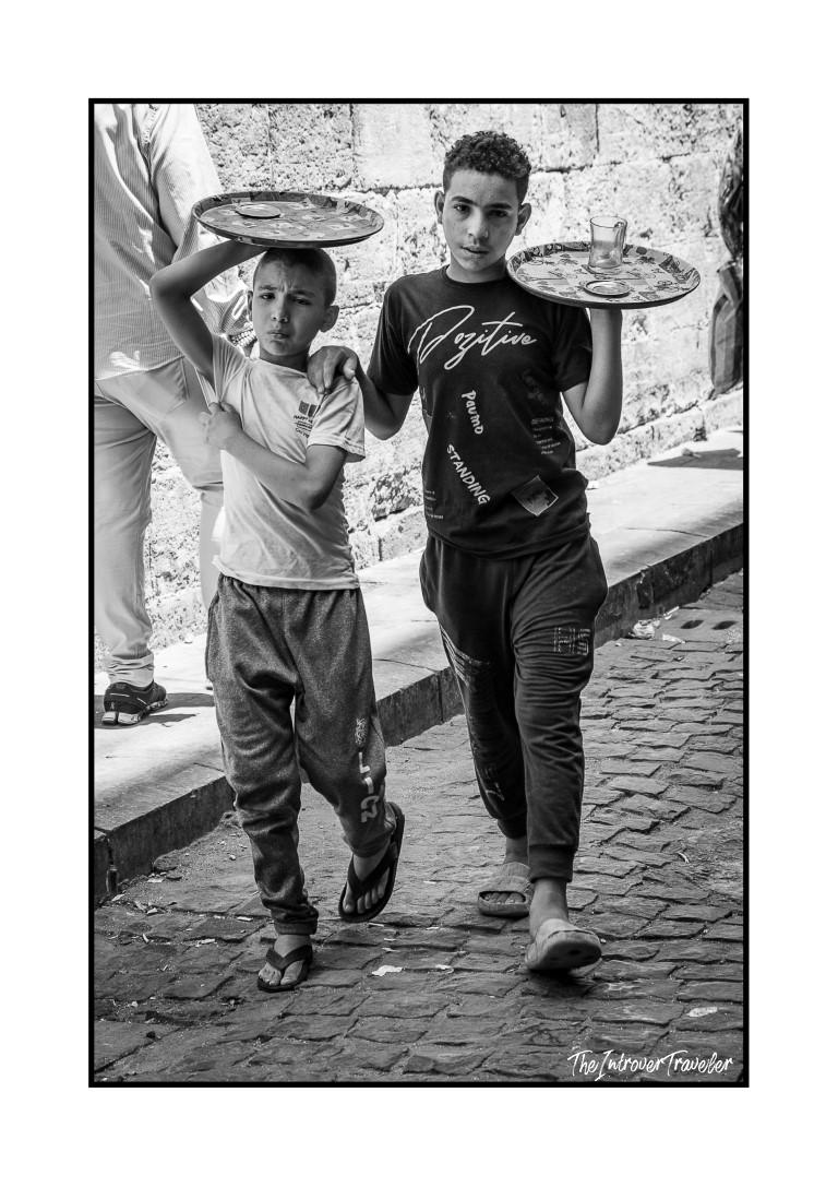 Two boys carrying tea trays through a cobblestone street in Egypt, candid street photography