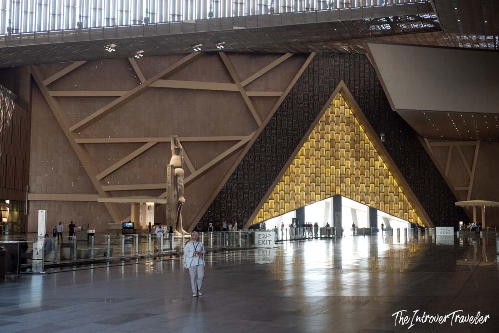 Grand Egyptian Museum atrium interior with glowing pyramid gateway and ancient Egyptian statue