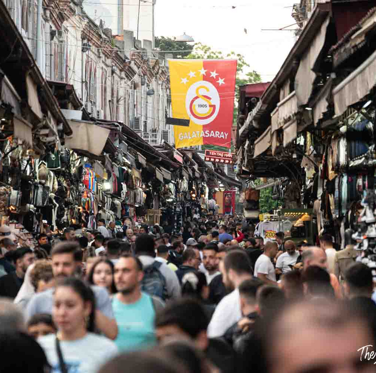 Crowded outdoor bazaar street in Istanbul with a Galatasaray football club banner overhead