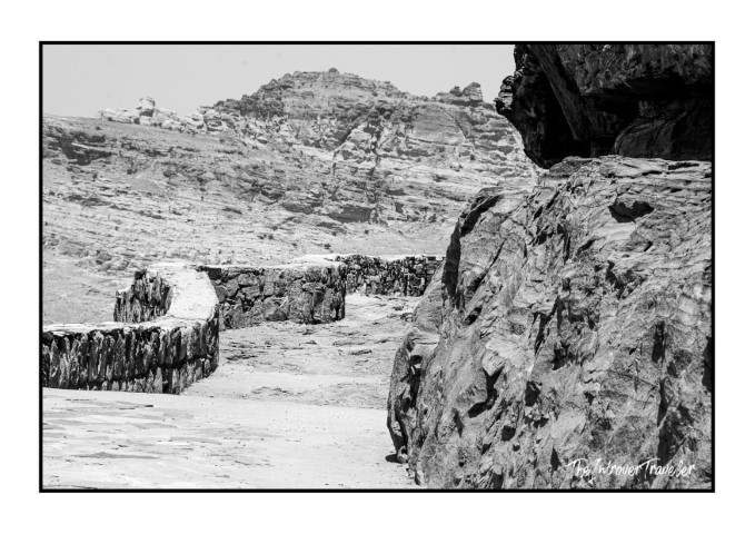 Black and white view of Petra's rocky desert landscape with ancient stone walls and rugged cliffs, Jordan