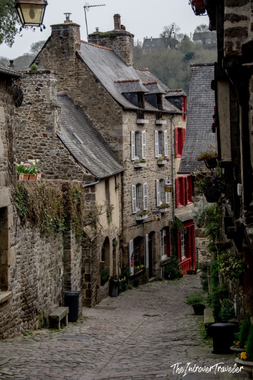 Cobblestone street in Dinan medieval village, lined with stone houses and red shutters in Brittany, France