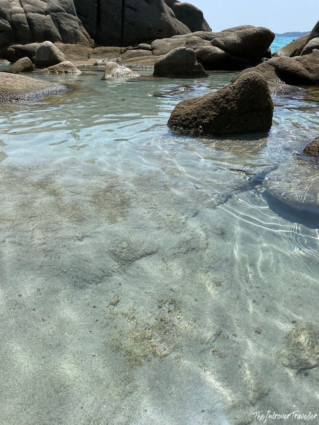 Crystal-clear shallow water over sandy seafloor with granite boulders, south Sardinia beach cove