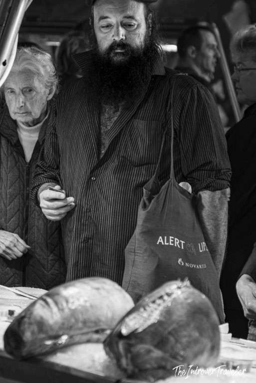 Bearded vendor and shoppers browsing fresh fish at a bustling coastal city market