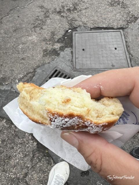 Hand holding a half-eaten Neapolitan sfogliatella dusted with powdered sugar, eaten street-side in Naples