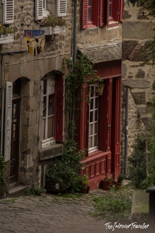Cobblestone street in Dinan's medieval old town with red shuttered stone buildings and ivy