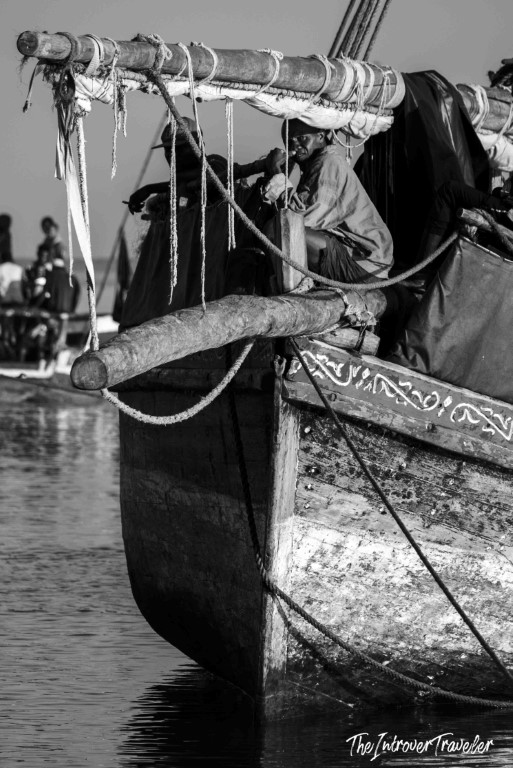 Black and white close-up of a traditional wooden dhow at a coastal fish market harbor