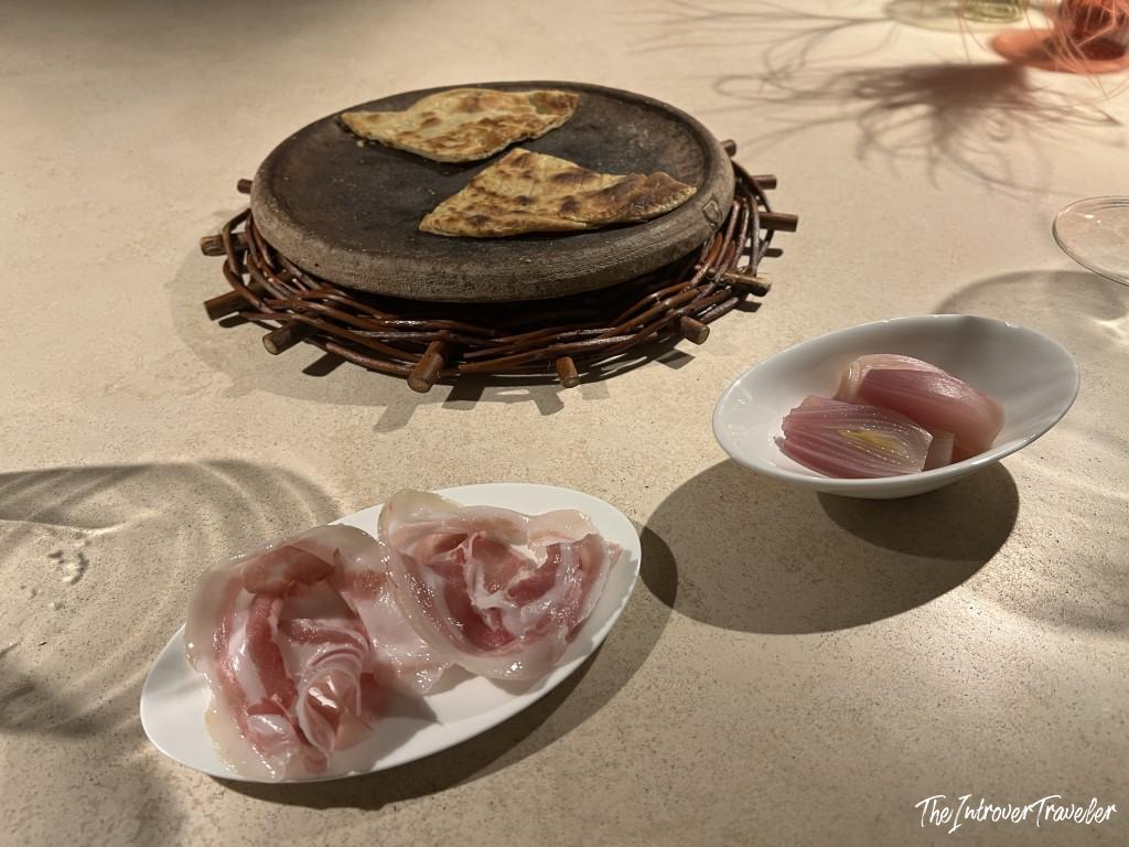 Toasted flatbread on stone plate, raw fish slices, and pickled shallots served at Trattoria Da Lucio, Rimini