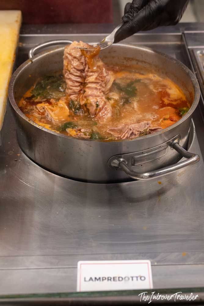 Lampredotto simmering in broth, lifted by a gloved hand at a Florence street food stall