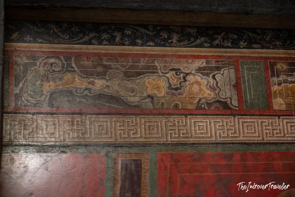 Faded decorative wall fresco with floral and geometric borders inside a Pompeii building