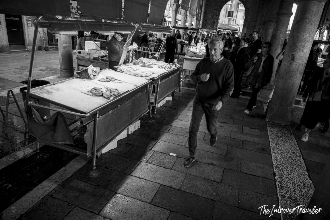 Busy fish stalls under stone arches at the Rialto Market in Venice, Italy