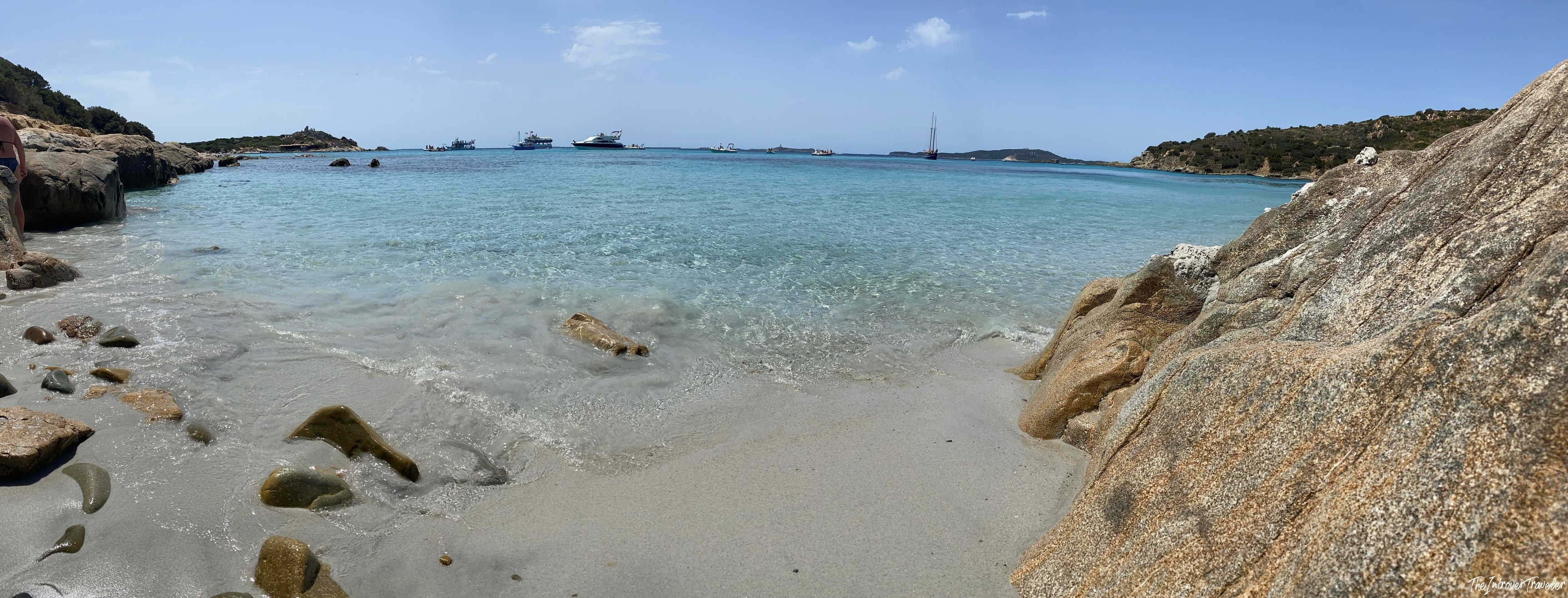 Secluded south Sardinia cove with crystal-clear turquoise water, granite rocks, and yachts anchored offshore