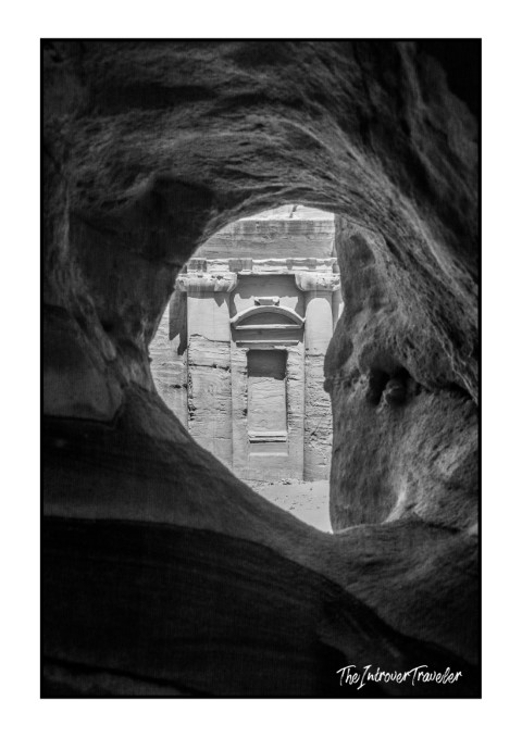 Nabataean tomb facade in Petra framed through a natural rock hole in the sandstone cliffs