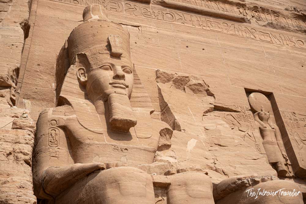 Close-up of a colossal Ramesses II statue at Abu Simbel temple facade, with hieroglyphic carvings above