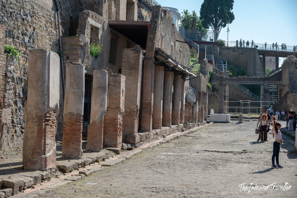 Ancient colonnaded street at Herculaneum excavations, with brick columns and tourists exploring the Roman ruins