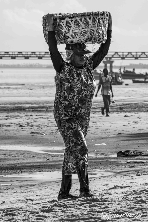 Woman carrying a woven basket of fish on her head at a coastal fish market beach