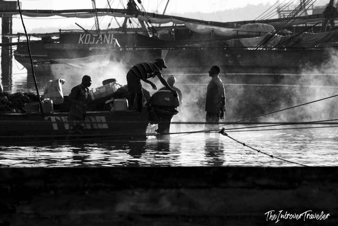 Fishermen unloading boats at a misty coastal fish market harbor, black and white