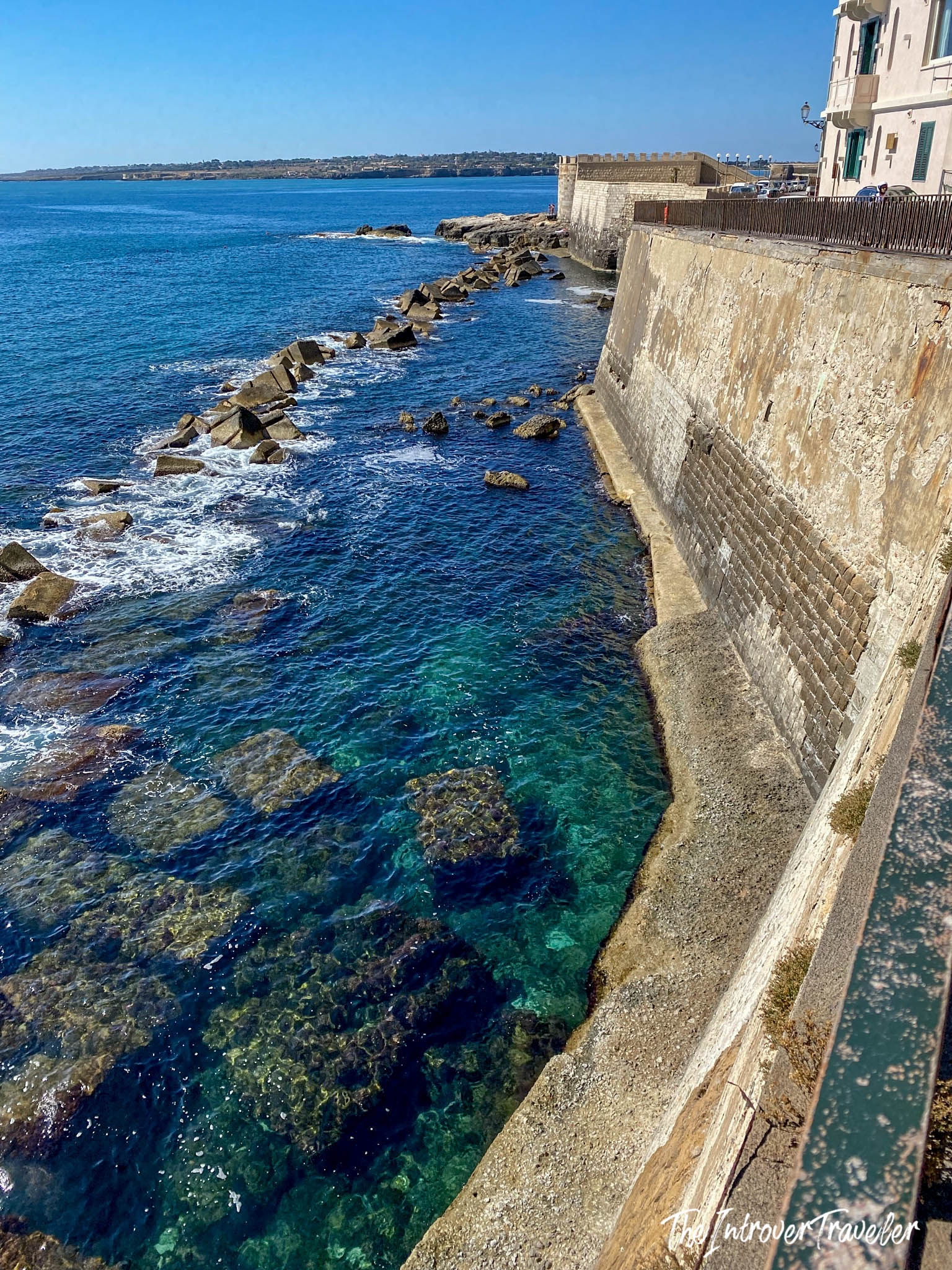 Ancient Norman sea walls of Ortigia rising above crystal-clear turquoise waters, Syracuse, Sicily