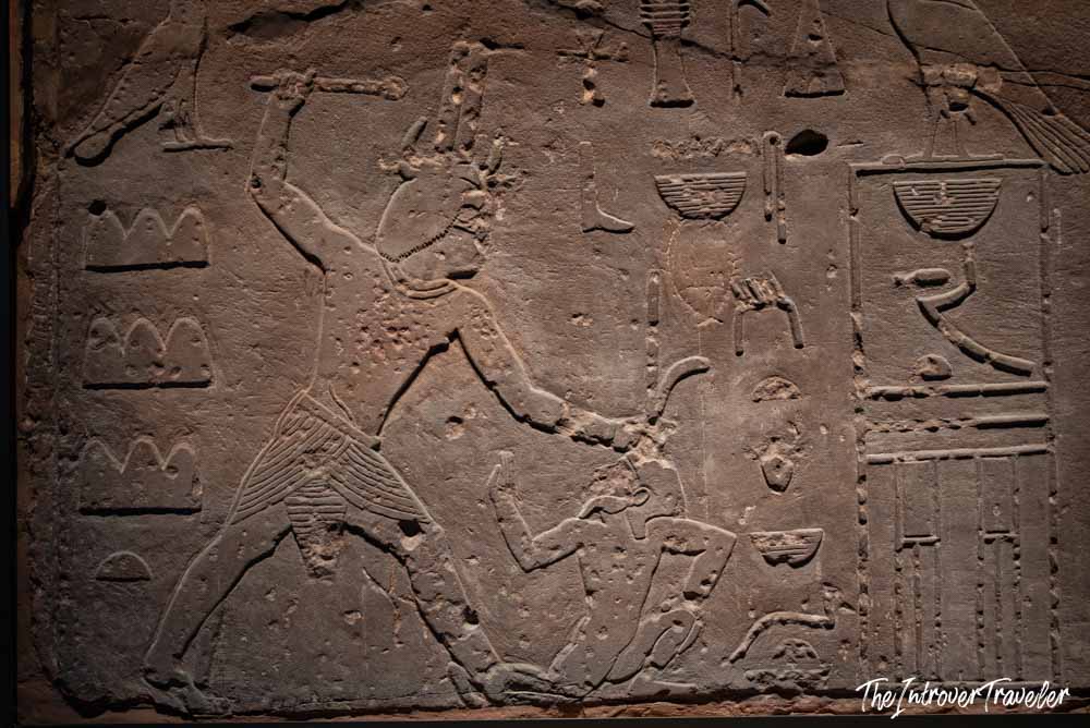 Ancient Egyptian stone relief carving showing a pharaoh smiting an enemy, Grand Egyptian Museum