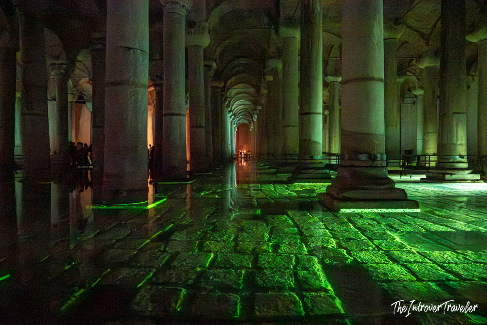 Interior of the Basilica Cistern in Istanbul, lit by green lights reflecting off ancient stone floors and columns