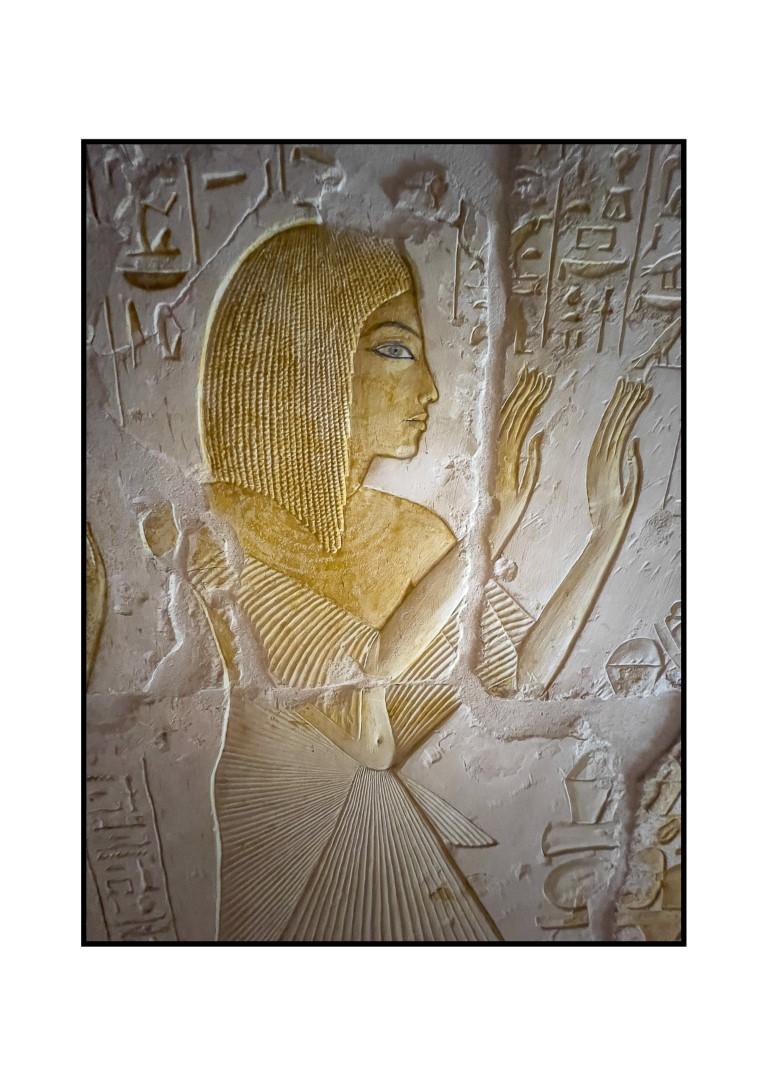 Ancient Egyptian painted relief showing a woman with golden wig, raised hands, and hieroglyphs carved in stone