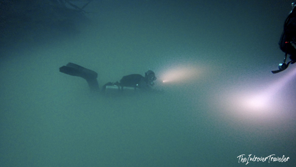 Scuba diver with torch light navigating murky underwater cenote in Yucatan, Mexico