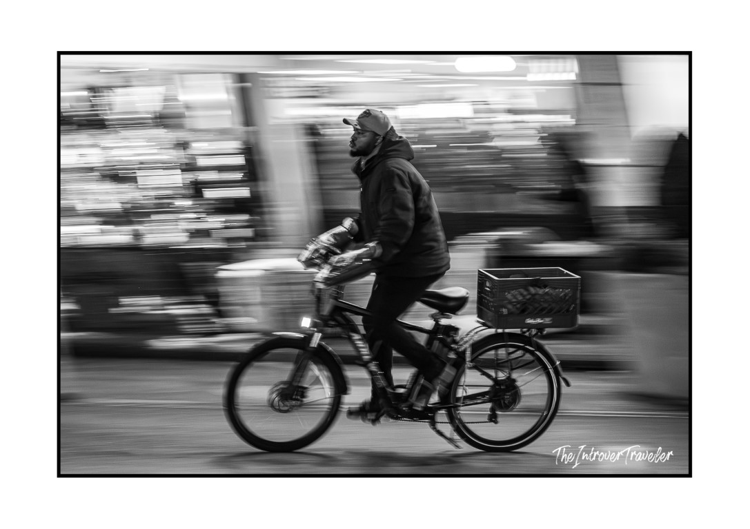 Black and white panned shot of a cyclist riding through busy New York City streets at night