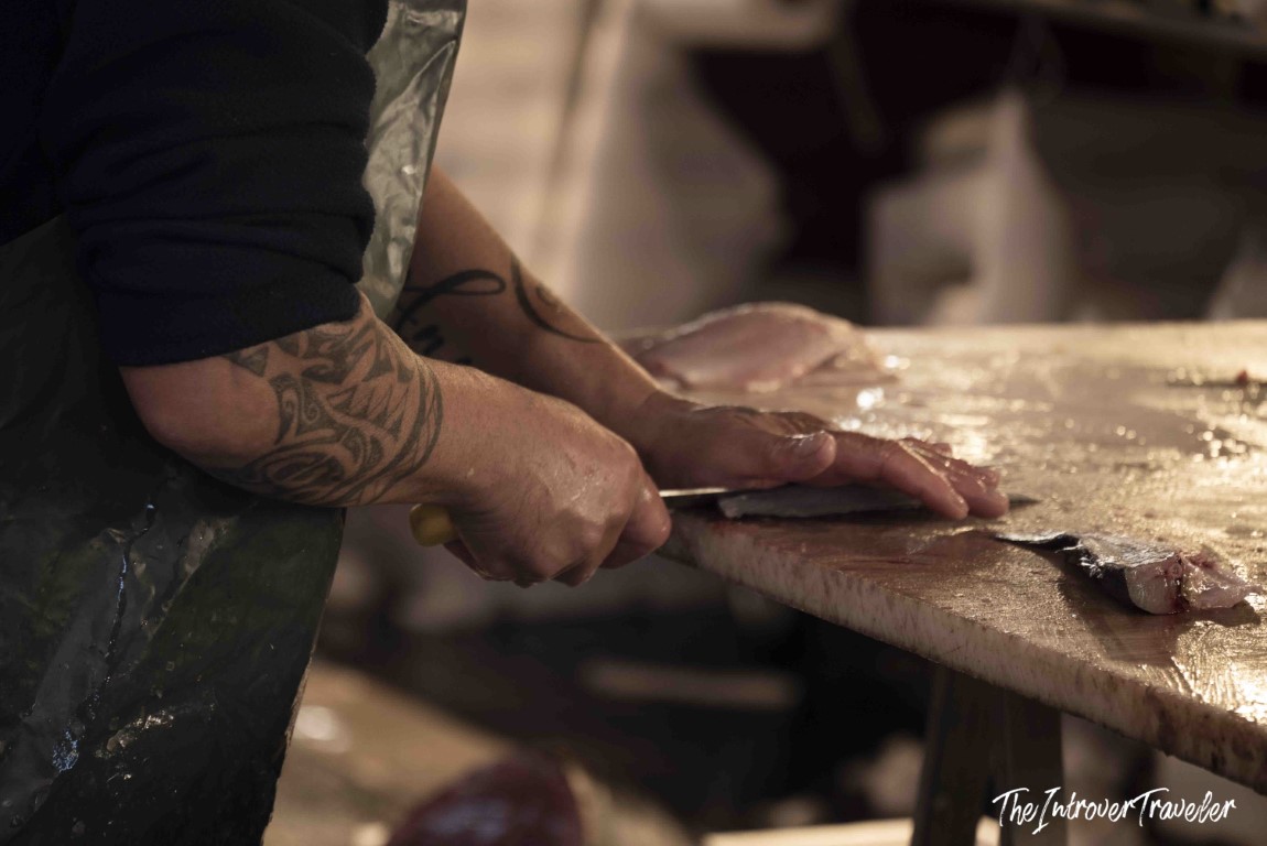 Tattooed fishmonger filleting fresh fish at a coastal city fish market