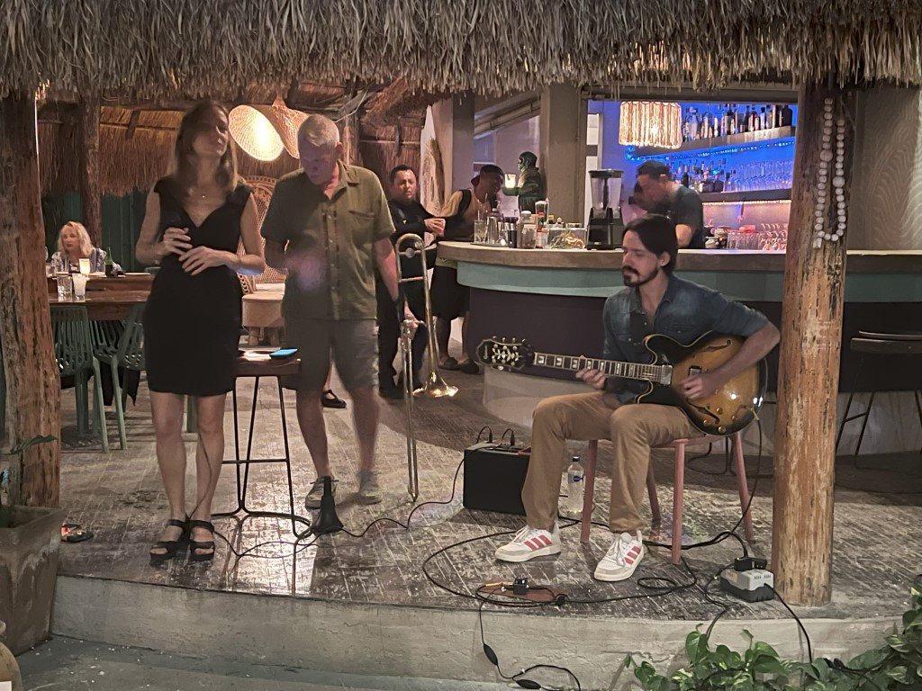 Live jazz band performing at Kondesa restaurant in Cozumel, with vocalist, guitarist, and trombone player under a palapa roof
