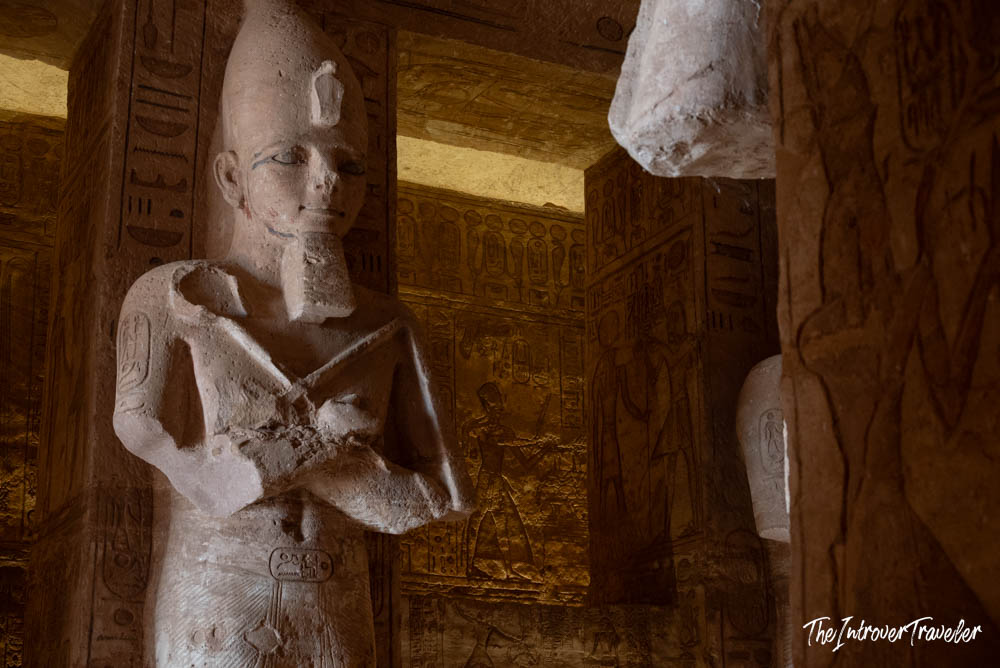 Osiride pillar statue of Ramesses II inside Abu Simbel temple, with hieroglyph-covered walls glowing golden