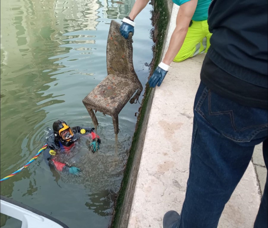 Diver retrieving a rusted chair from a Venice canal during an underwater cleanup operation