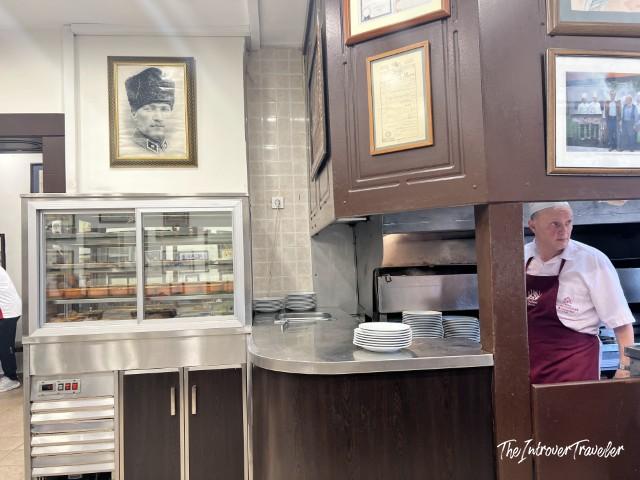 Interior of Sultanahmet Köftecisi restaurant with Ataturk portrait, display case, and staff at counter