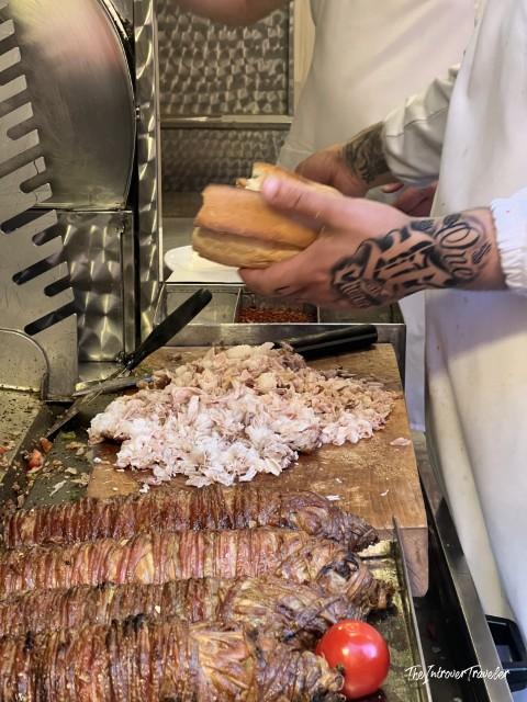 Tattooed vendor chopping kokoreç on a grill at Güneş Kokoreç in Istanbul