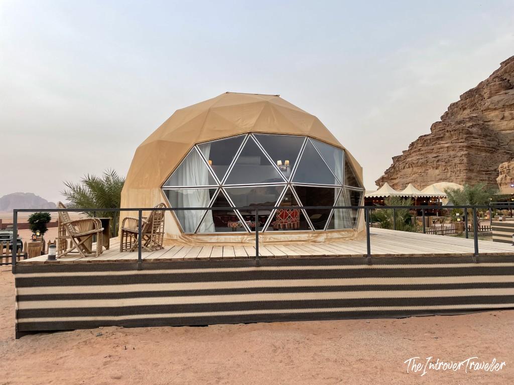 Geodesic dome glamping tent with wooden deck amid Wadi Rum desert sandstone cliffs, Jordan